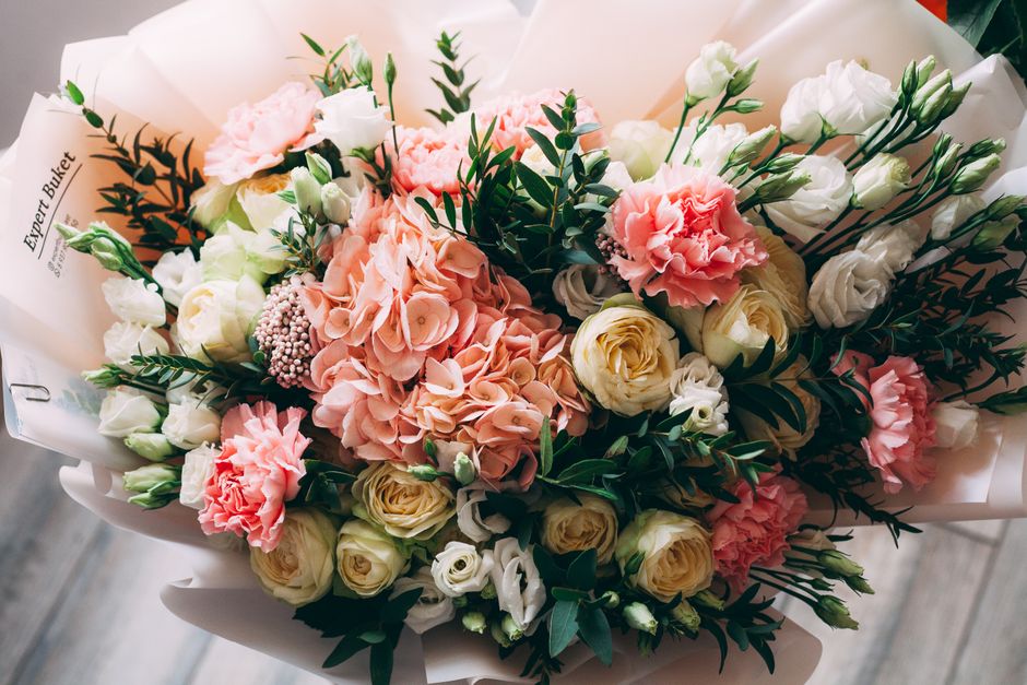 A delicate bouquet featuring soft pink hydrangeas, white roses, and pink carnation flowers, accented with green foliage and eucalyptus stems. The arrangement is wrapped in elegant white paper, tied wi