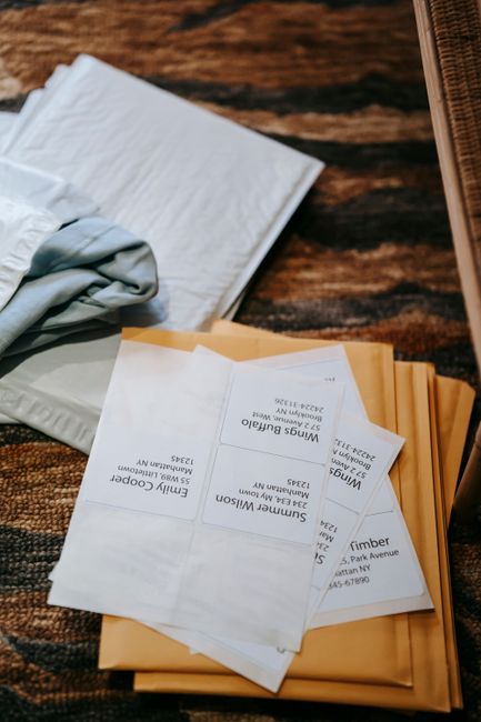 An overhead view of a neatly arranged workspace featuring a stack of white and light blue tissue paper, alongside a partially open yellow mailing envelope containing multiple printed flower delivery o