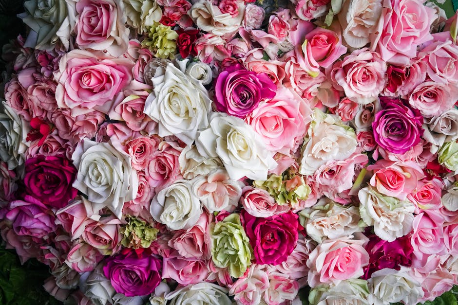 A dense arrangement of fresh roses in various shades of pink, white, and deep magenta, with some pale green blooms and buds interspersed. The roses have velvety petals, with some fully open and others
